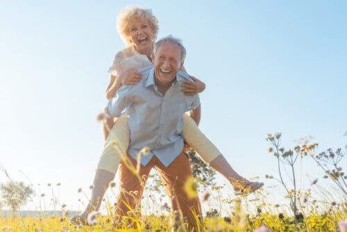 older man giving piggy back ride to older woman in field | Remember That Presence Is the Real Present